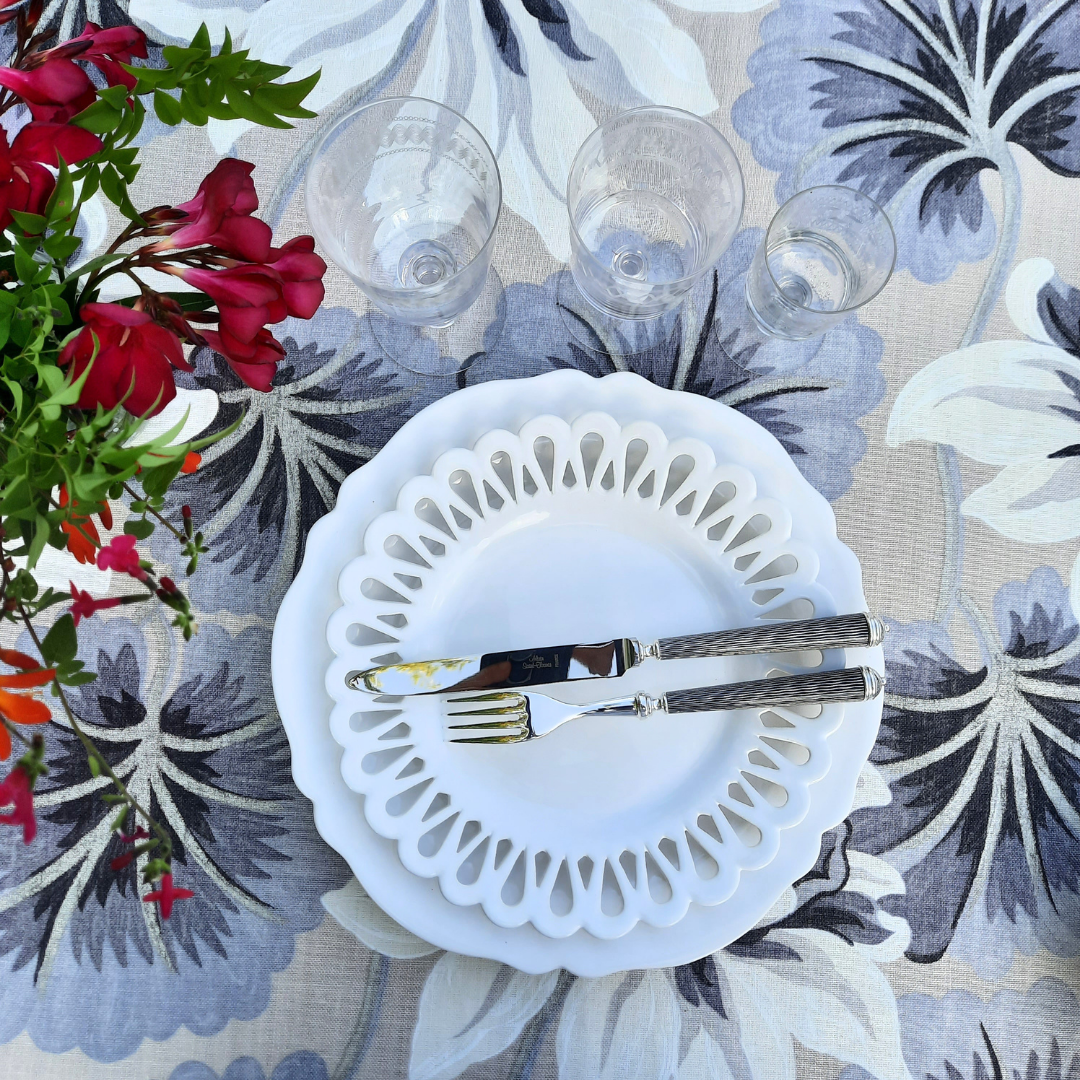 Chevet openwork white salad plate and a Feston dinner plate in white on a patterned table cloth with cutlery and ref flowers