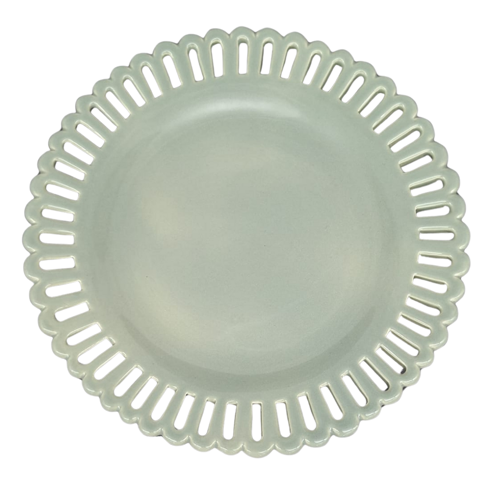 A sage green round ceramic cake plate on a low foot with a scalloped, openwork rim featuring elongated slit-like cutouts, shown from a top-down view on a white background.
