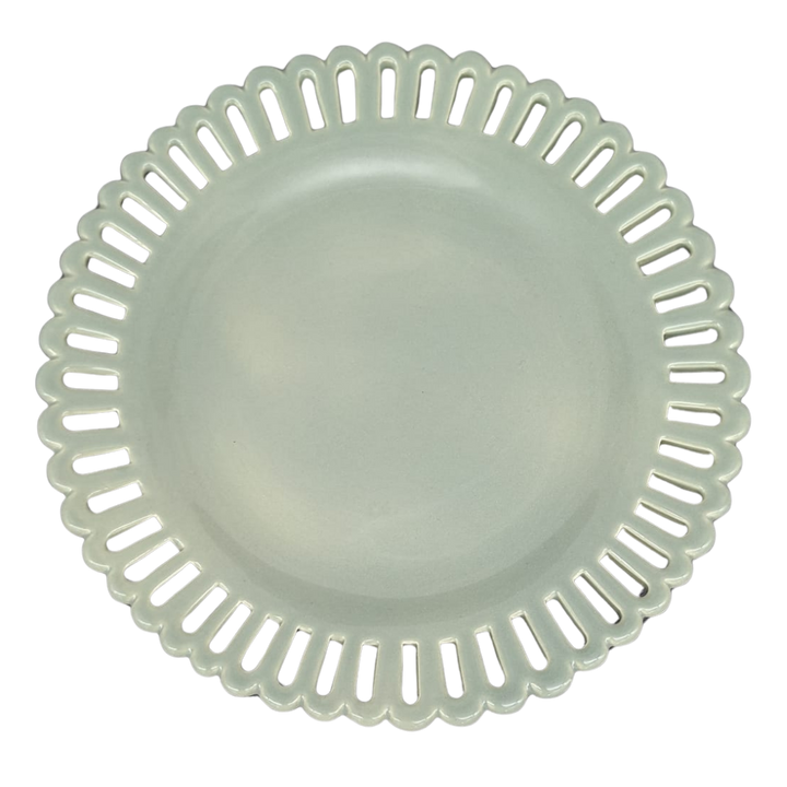 A sage green round ceramic cake plate on a low foot with a scalloped, openwork rim featuring elongated slit-like cutouts, shown from a top-down view on a white background.