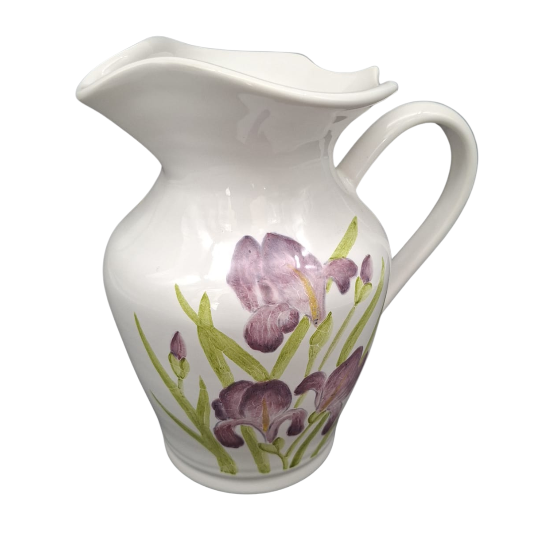 A white ceramic pitcher decorated with a hand-painted floral design of purple irises and green leaves, shown against a plain white background.