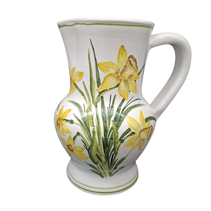 A white ceramic pitcher decorated with yellow daffodils and green leaves, shown against a plain white background.